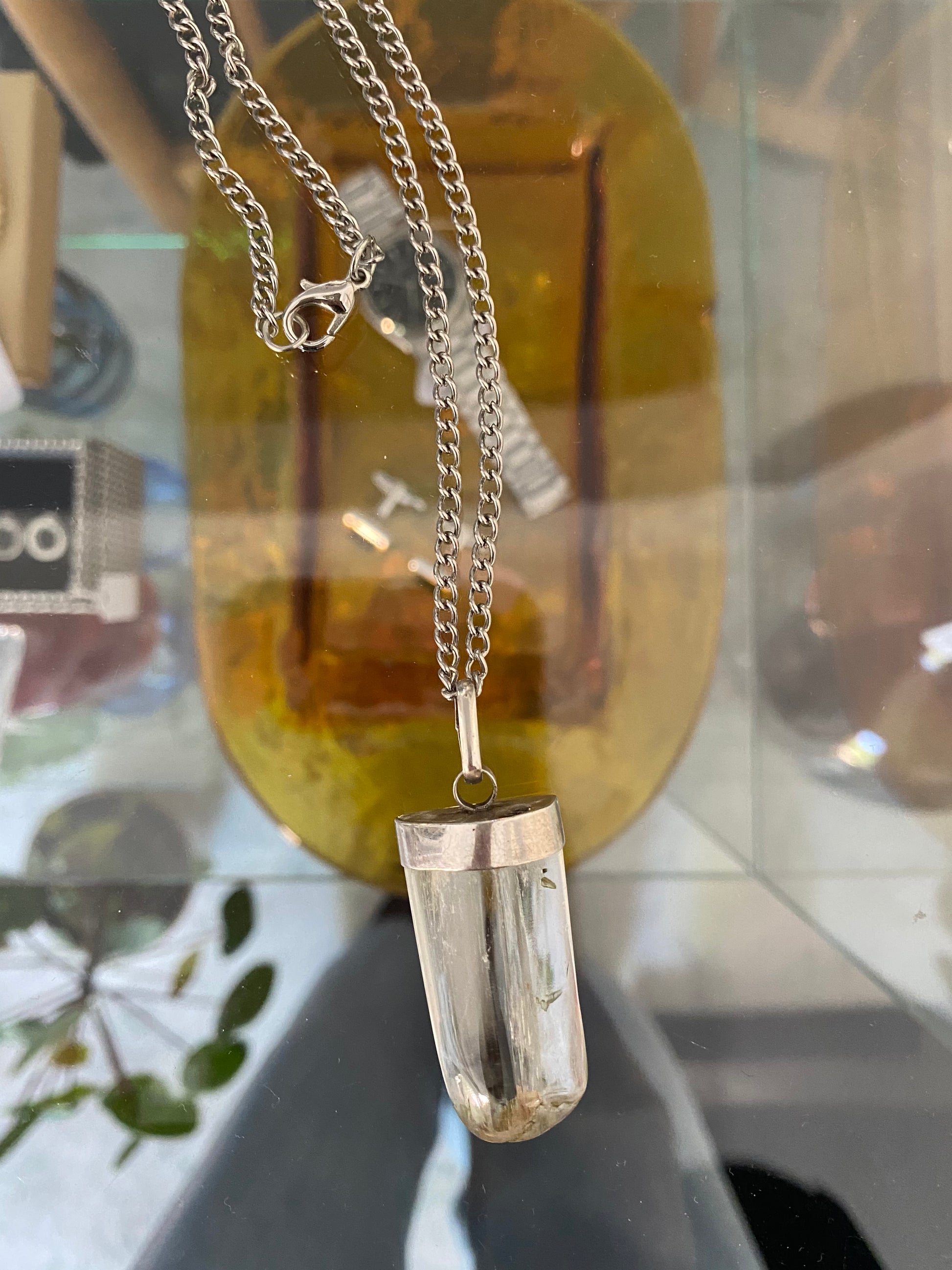 Silver necklace with a rock crystal pendant on a reflective surface